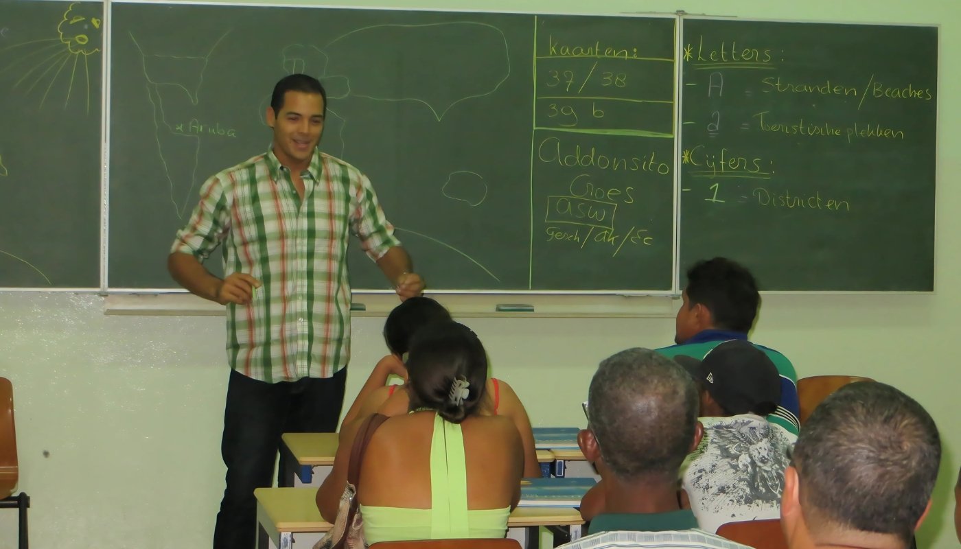 Teacher giving a geography an example lesson to parents of students in a classroom at Filomena Mavo College, with a chalkboard showing maps and notes in Dutch.