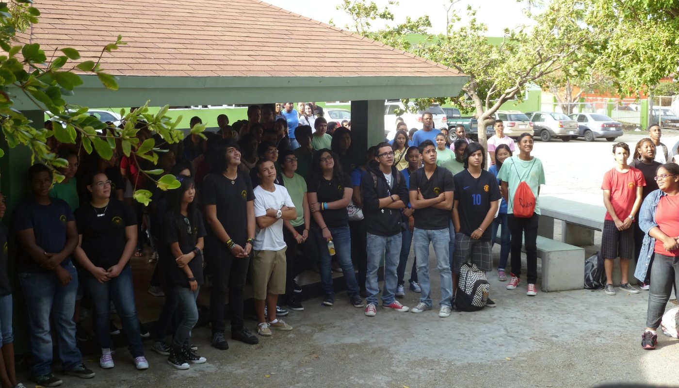 Students of Filomena Mavo College gathered outside during a school event for 18 march in 2012, attentively watching a presentation or speech.