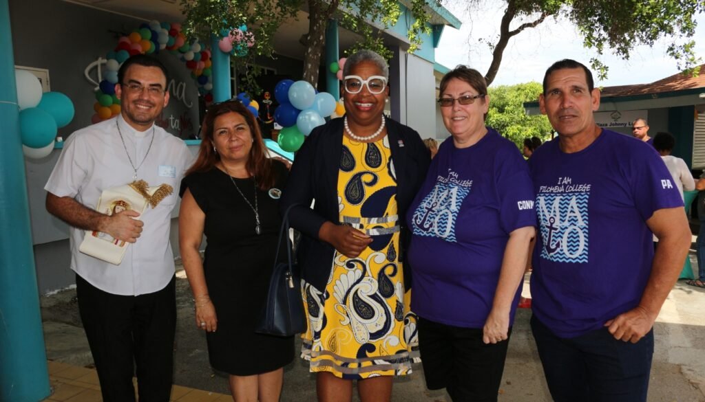 Group photo of Filomena Mavo College staff and guests smiling in front of a decorated school entrance during a celebration or special event.