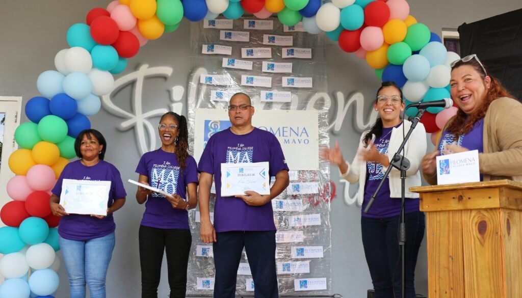 Filomena Mavo College teachers smiling and holding certificates during a jubilee ceremony under a balloon arch.