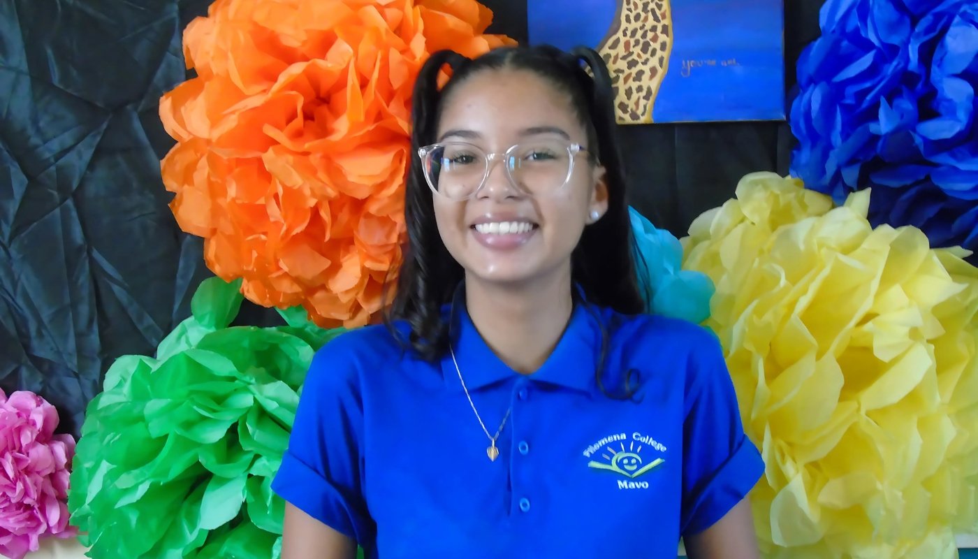 Smiling female student in a blue Filomena Mavo College polo shirt posing in front of a colorful paper flower background.